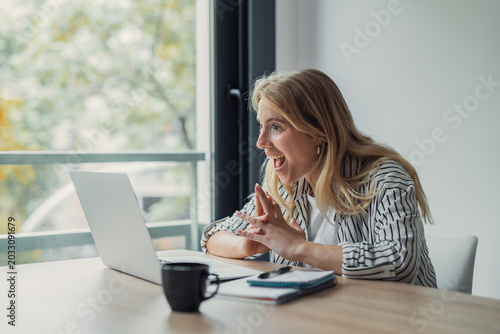 Tableau sur toile Young woman in her 20s at a home office desk, clasping hands and smiling with mo