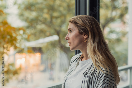 Foto Young woman in a striped shirt and gold earrings gazes out a window in natural d