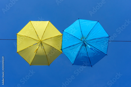 two colourful umbrellas, one blue and one yellow, hanging from a rope against the backdrop of a blue sky on a sunny day