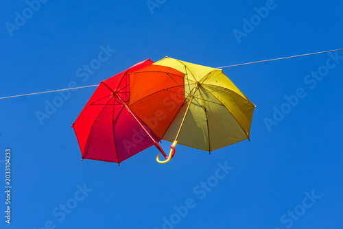 two colourful umbrellas, one red and one yellow, hanging from a rope against the backdrop of a blue sky on a sunny day