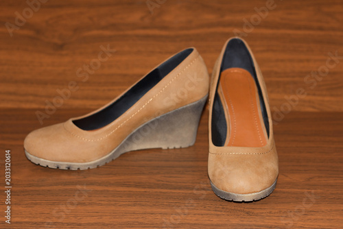 A pair of stylish women's tan wedge heel shoes sit on a dark wood grain surface.