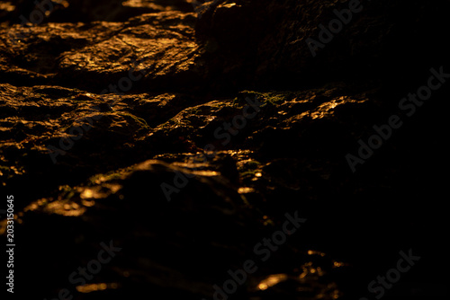 Macro photography of a textured black stone with dramatic sunlight casting sharp natural shadows, revealing fine surface details and strong contrast in a minimalist composition.