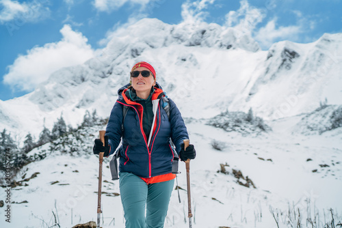female climber with trekking poles and backpack under Eisenerzer Reichenstein mountain in Austria representing winter alpinism extreme outdoor sports and active lifestyle