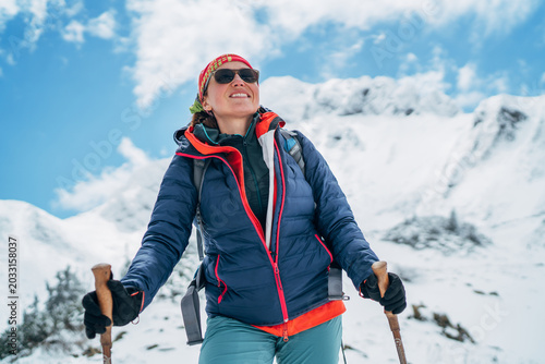 smiling female climber with trekking poles and backpack under Eisenerzer Reichenstein mountain in Austria representing winter alpinism extreme outdoor sports and active lifestyle