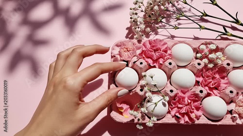 Womans hand arranging eggs in a decorated carton with flowers