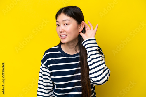 Quadro su tela Young Chinese woman isolated on yellow background listening to something by putt