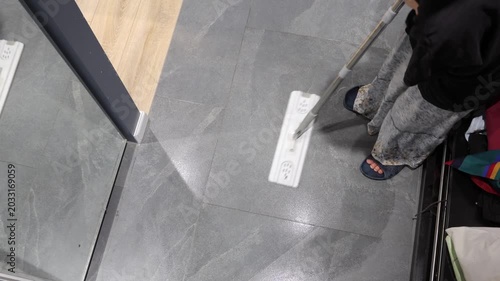 A flat mop cleans gray tile at the threshold between the entryway and a light wooden floor.