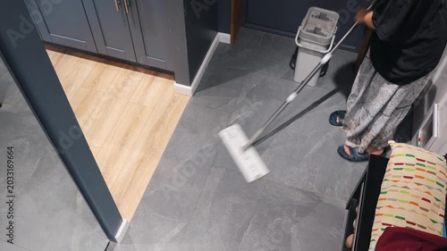 A teenager cleans gray tile beside dark cabinets as part of an indoor home cleaning routine.