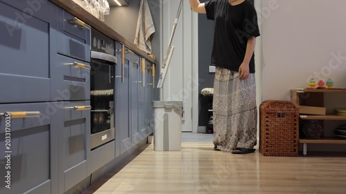 A teenager mops a light wooden floor beside blue kitchen cabinets during a home cleaning routine.