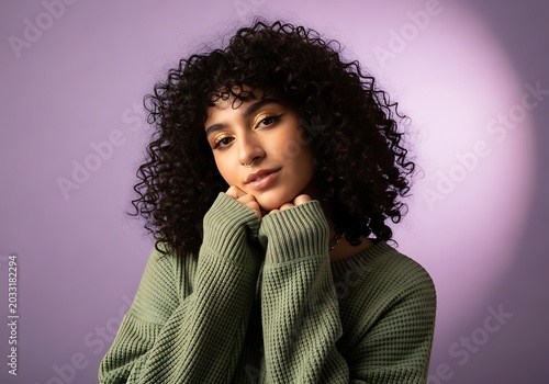A curly haired woman posing in a green sweater in a purple studio with soft lighting and gold makeup