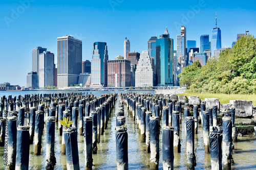 Tableau sur toile Abandoned wooden pier pilings in East River with Lower Manhattan skyline and One