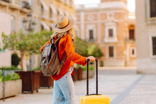 Foto A young tourist with a yellow suitcase and backpack walks through a sunny city square