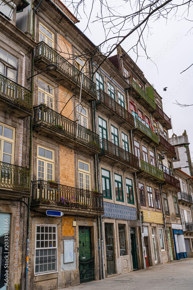 Fototapeta premium Row of historic residential buildings in Porto featuring ornate iron balconies, colorful facades, and traditional ceramic tile details in an old European street.