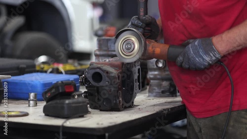 A mechanic diligently cleaning a truck cylinder head with a grinder in a well-lit, professional garage. The scene captures the precision and tools of automotive repair.