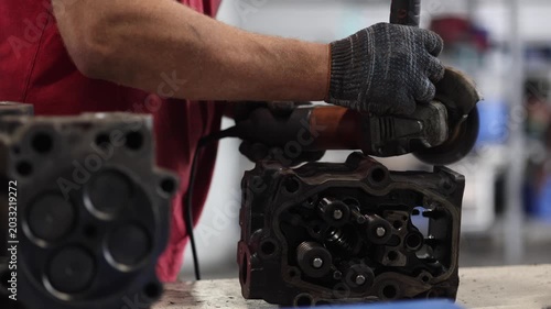A skilled mechanic is meticulously cleaning a truck cylinder head using a grinder in a well-equipped maintenance shop. The scene showcases the professionalism and expertise in automotive repair.