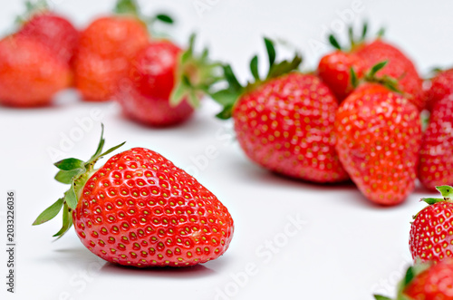 Close up of a fresh red strawberry on white background with blurry strawberries in selective focus
