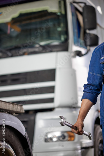 A skilled mechanic in blue overalls confidently holds a wrench, symbolizing expertise in quality truck repairs. The image captures dedication and professionalism in automotive maintenance.