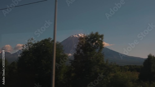 Breathtaking view of volcano and its peak in clouds and with snow on slopes. Heavy traffic on highway with power line running alongside. Vertical video.