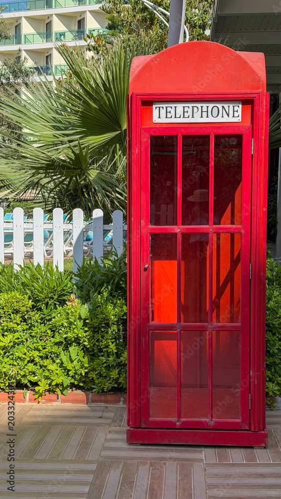 Obraz premium Classic Red British Telephone Booth In Tropical Luxury Resort With Palm Trees And Summer Vacation Atmosphere.