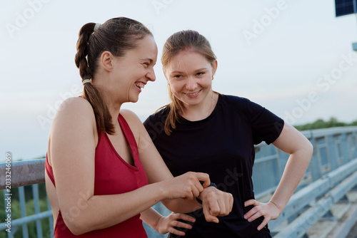 фотографія Two friends stand on a bridge during the evening, smiling and chatting as one checks a smartwatch