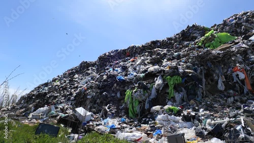 Workers collect trash near a large mound of garbage at an abandoned dump in an area filled with pollution and waste materials