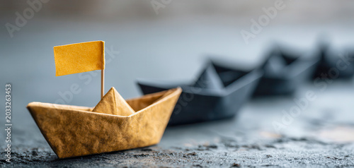Paper boats float on a surface with a gold flag while other paper boats sit lined up in the background