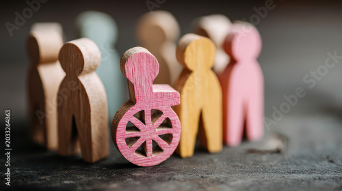 Wooden figures in various shapes gather around a wheelchair on a wooden surface during daylight hours