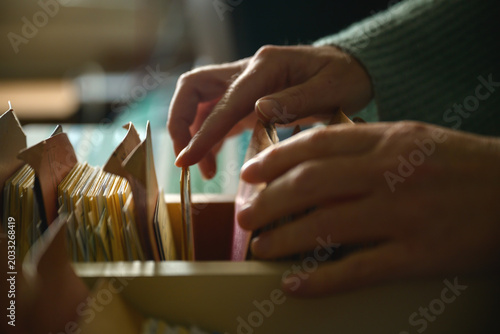 Close-up of female hands browsing old card catalog drawers, vintage library research concept