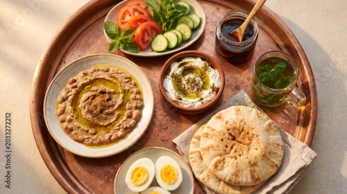 Middle Eastern breakfast spread with hummus, pita, vegetables, eggs on wooden tray
