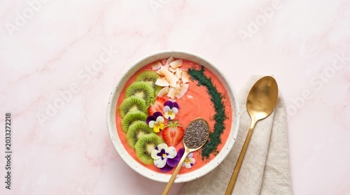 Colorful smoothie bowl with fresh fruit, edible flowers, seeds on pink marble