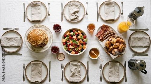 Breakfast table setting overhead view with fruit, pastries, bacon