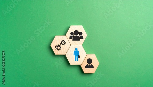 Wooden hexagonal blocks arranged in a pyramid with black human icons and one blue figure at the top on a green background, symbolizing leadership, hierarchy, and team organization.