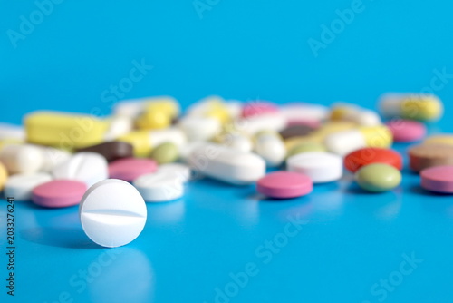There are many multi-colored medicine tablets on a blue background.