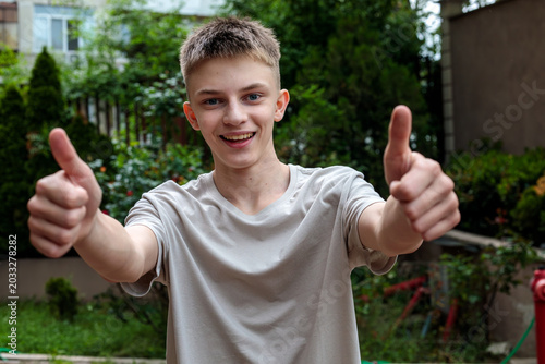 Happy teenage boy showing double thumbs up gesture outdoors in garden, approval and positive reaction, youth lifestyle concept