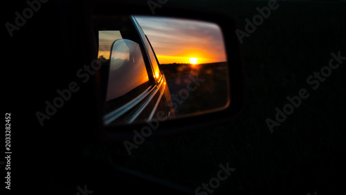 Car mirror reflection of sunset landscape and vehicle fragment on a dark background web banner.