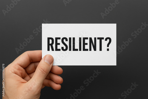 Hand holding white card with text resilient presenting determined confident business continuity organization resilience concept and crisis preparedness question on stark black background