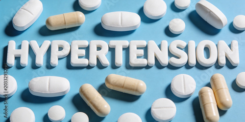 Hypertension word made of pills on blue background. Treatment of high blood pressure and cardiac disease. Medical concept of pill medication for cardiovascular system health care support.