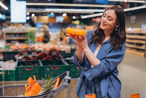 Fotografie Woman holding fresh orange tomatoes, smiling while shopping for produce in a bri