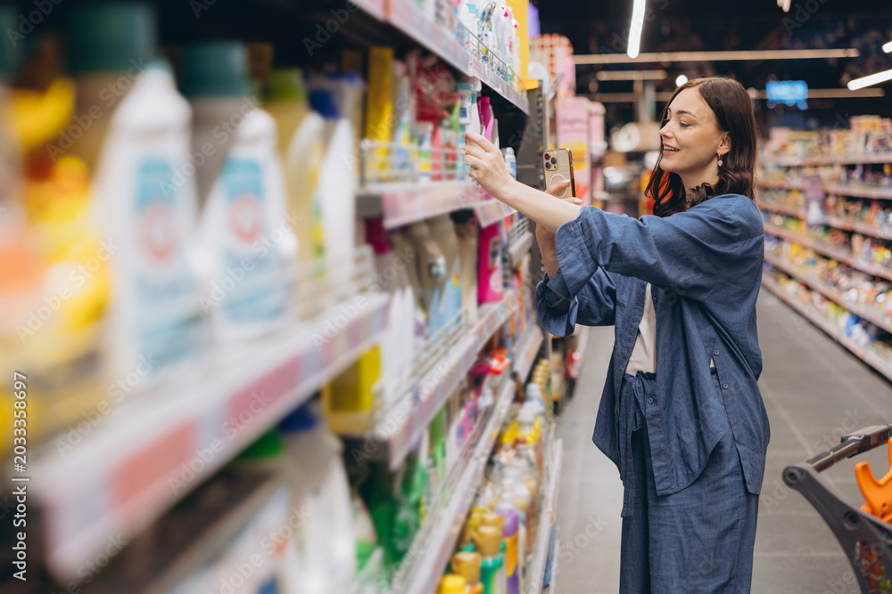 Obraz premium Woman scanning product QR code with smartphone at supermarket, making informed purchasing decisions