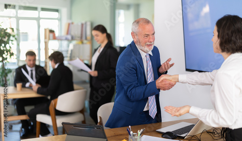 Bilde på lerret Elderly male bank manager shakes hand with adult woman client during business me
