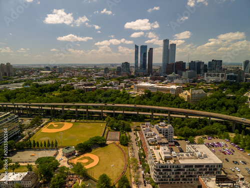 Jersey city urban landscape extending with skyscrapers and residential buildings along the coastline. Showing multiple baseball fields and elevated highways