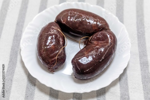 Three traditional blood sausages (morcela, chouriço) served on a white plate over a striped tablecloth.