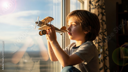 Young boy holding toy airplane at window, childhood dream, imagination, sunlight, photo
