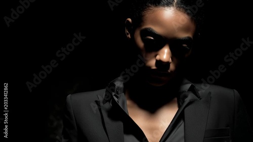 Model poses in dramatic lighting during a photoshoot in a studio setting with strong contrasts and shadows on her face at night