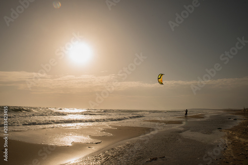 Silhouette of a kite surfer on the beach flying a kite at sunset