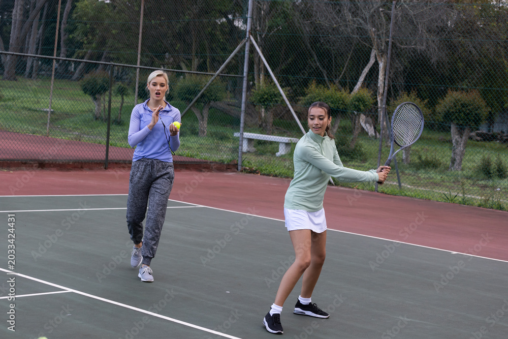 Obraz premium Two female partners practicing on park court in sneakers, holding racket and ball, copy space
