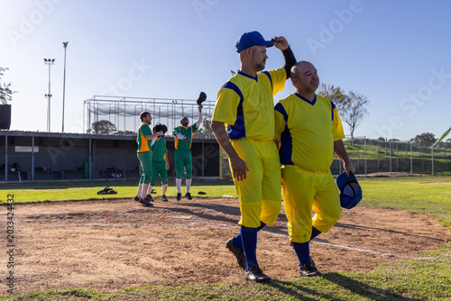 Obraz na plátně Vertical video: Walking two in yellow uniforms off infield after play holding bl