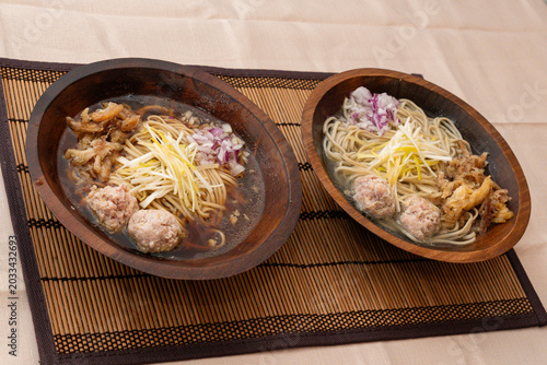 Photograph of two plates of traditional ramen in a wooden bowl on a bamboo tablecloth