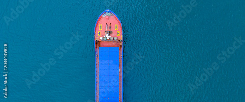 Extreme top down drone capture focusing specifically on the rounded red bow and leading blue cargo bays of a heavy marine transport vessel floating alone on a vast expanse of dark blue water