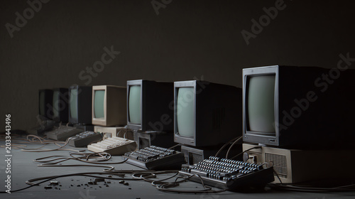A row of vintage computer monitors and keyboards, showcasing the evolution of technology against a dark background.